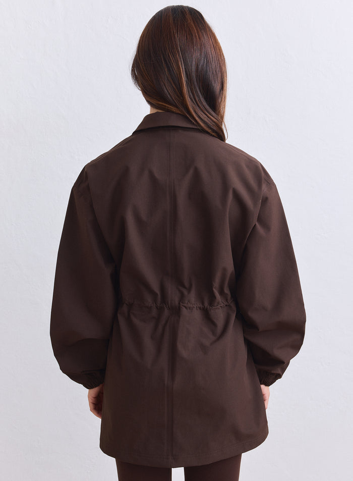 Back view of a chocolate brown aim'n waterproof jacket with a cinched adjustable waist. [S-165cm]