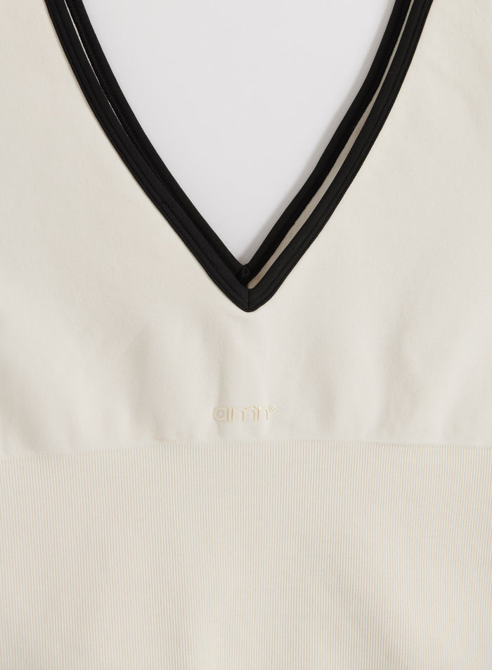 Cream Shape Seamless Deep Cut Singlet featuring a black V-neck trim and embossed aim'n logo.