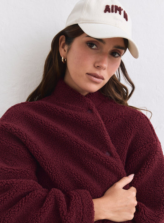 Cream cotton Campus Cap with burgundy aim'n embroidery worn with a textured burgundy jacket.