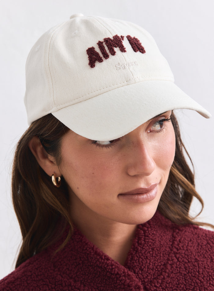 Cream cotton Campus Cap featuring a textured burgundy aim'n logo and white embroidery.