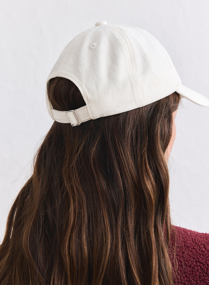 Back view of a cream cotton Campus Cap from aim'n worn over long wavy hair