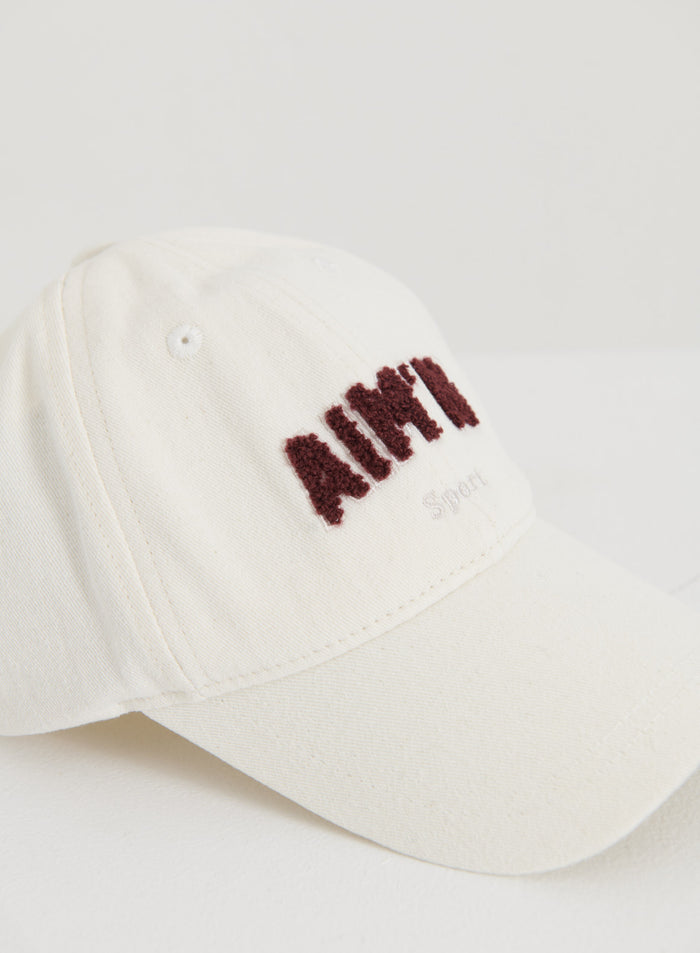 Cream cotton campus cap featuring textured burgundy aim'n logo embroidery and a curved brim.