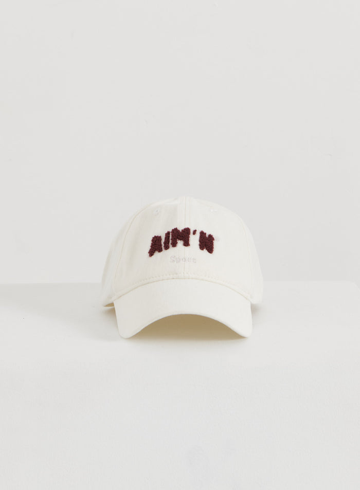 Cream cotton Campus Cap with a dark red fuzzy aim'n logo, presented in a minimalist flatlay style.