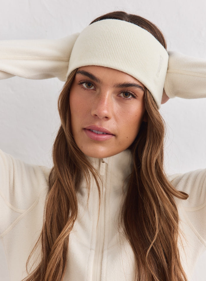 Woman wearing a cream knitted aim'n Outdoor Logo Headband with a matching fleece jacket.