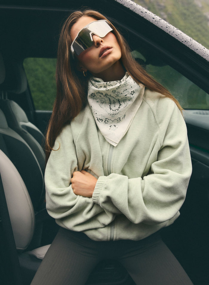 Model wearing a cream outdoor scarf and a light green jacket inside a car