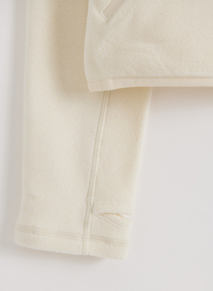 Close-up flatlay of a cream stretch fleece zip jacket showing its soft fleece texture, sleeve, seam and hem details