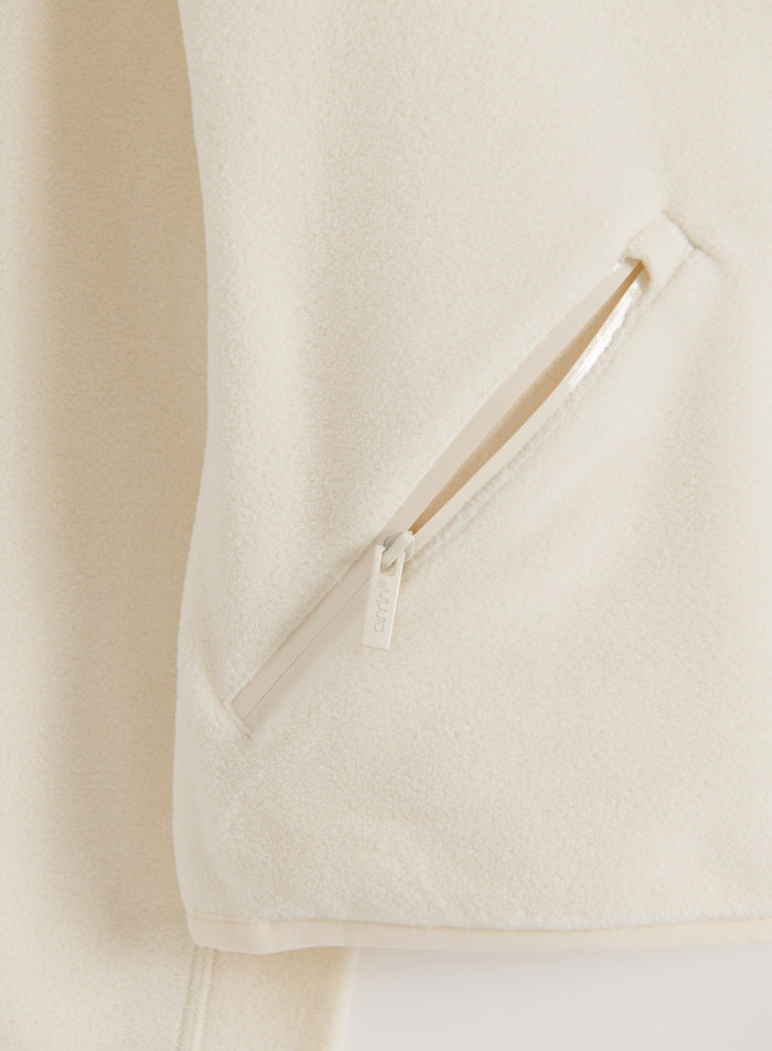 Close-up of a cream stretch fleece zip jacket showing the soft fabric texture and front zipper