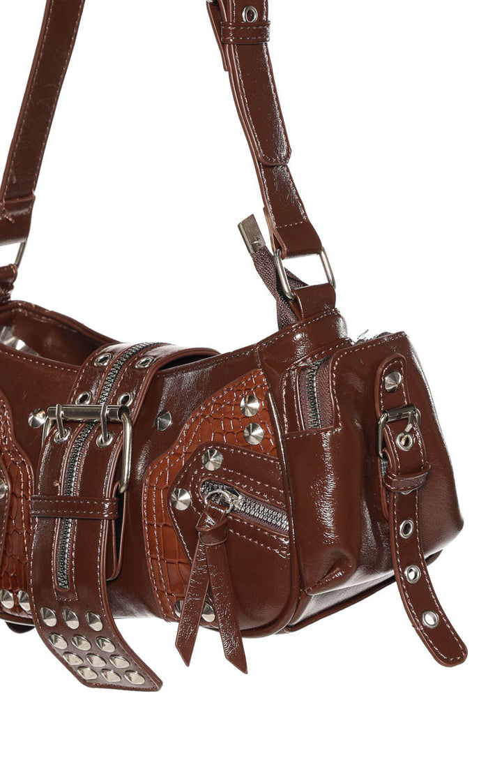 Angled close-up of brown PU shoulder bag with silver hardware, multiple zippers, studs, and crocodile embossed panels