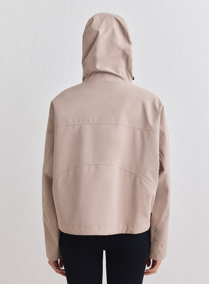 Rear view of a dark clay aim'n Waterproof Jacket featuring an adjustable hood and cropped fit. [M-178cm]