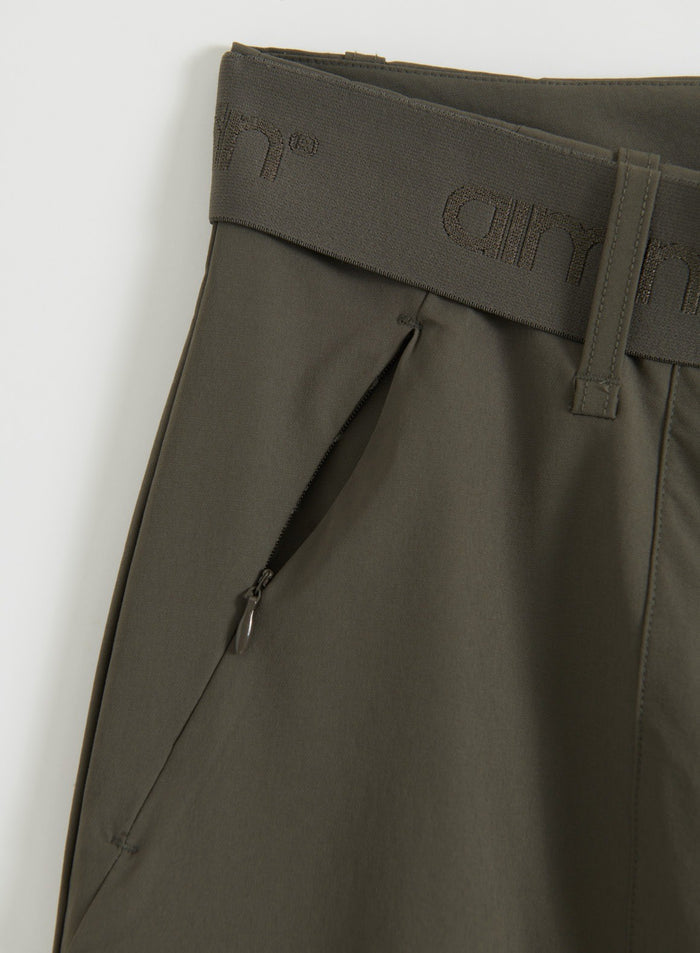Close-up of Dark Ivy cargo pants showing the high waistband, adjustable logo belt, and zipped hand pocket