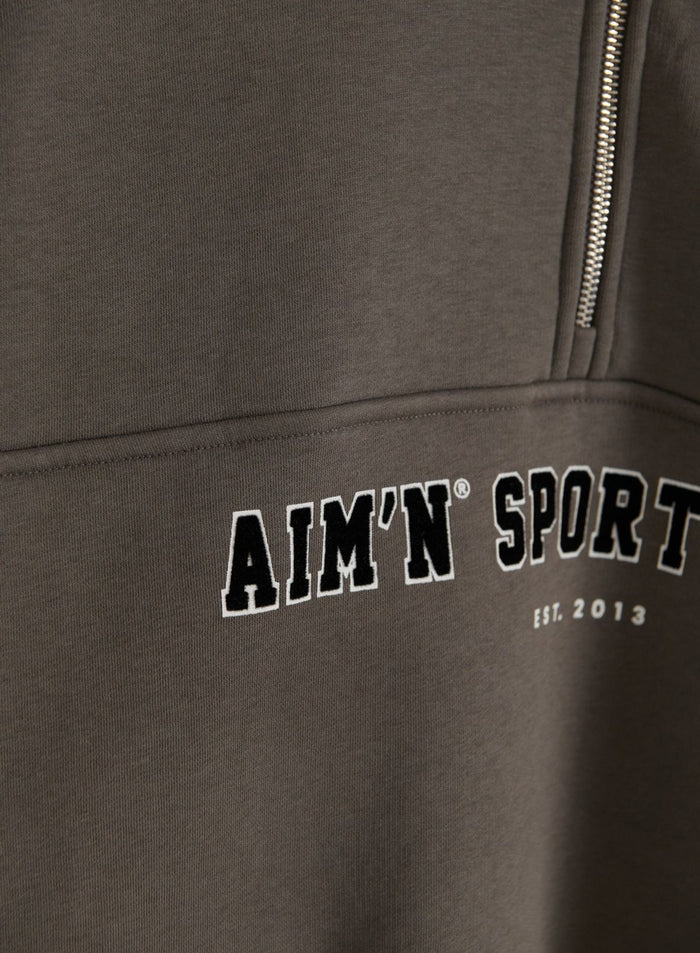 Close-up of the dark ivy Varsity Sweat Half Zip showing the zipper, soft fabric and aim'n varsity chest embroidery