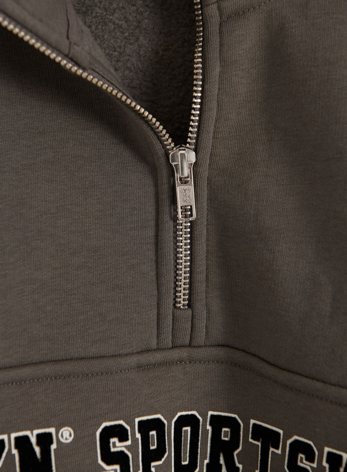 Close-up of the dark ivy Varsity Sweat Half Zip showing the brushed interior, silver half-zip closure and partial aim'n varsity print