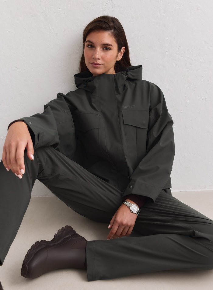 Dark ivy aim'n Waterproof Jacket with cargo pockets worn by a model sitting on the floor. [M-178cm]