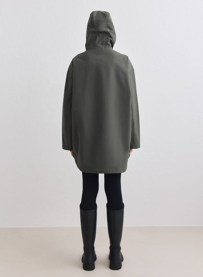 Dark ivy waterproof oversized anorak featuring a hood, shown from the back with black rain boots. [M-178cm]