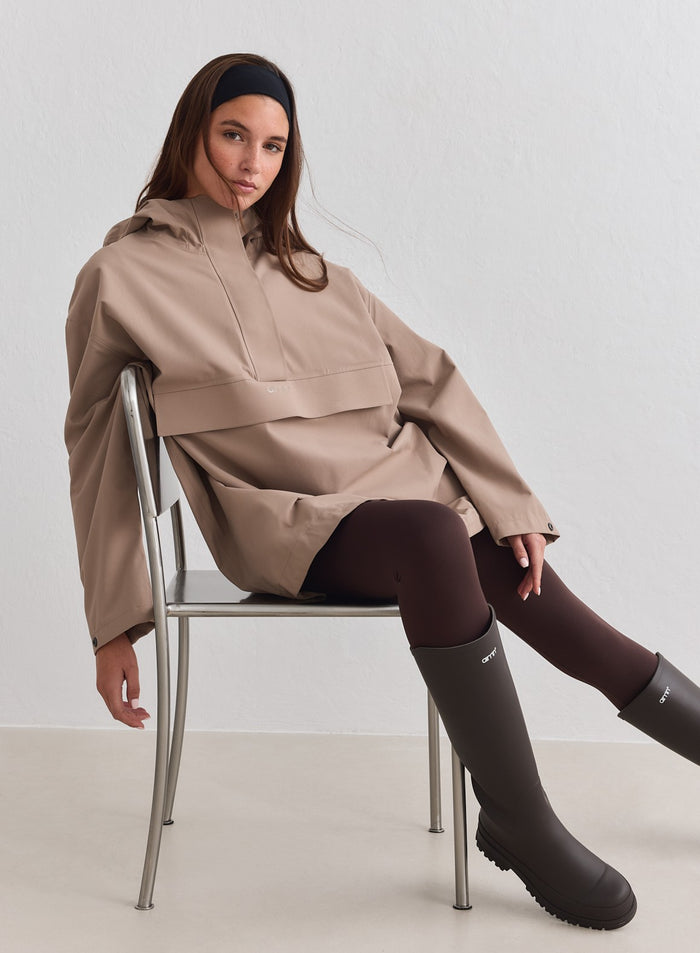 Model wearing Espresso Waterproof Oversized Anorak while sitting on a chair [M-178cm]