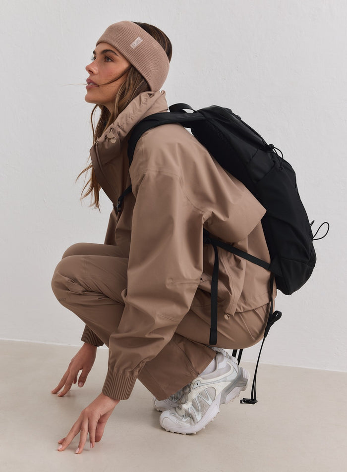 Hazelnut ribbed knit headband with an aim'n logo, styled with a matching outdoor set and black backpack.