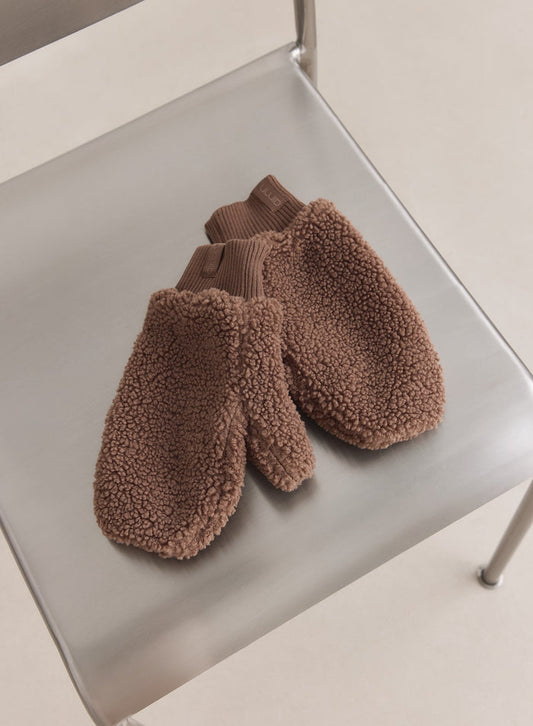 Hazelnut pile mittens from aim'n featuring a fuzzy texture and ribbed cuffs, resting on a metal chair.