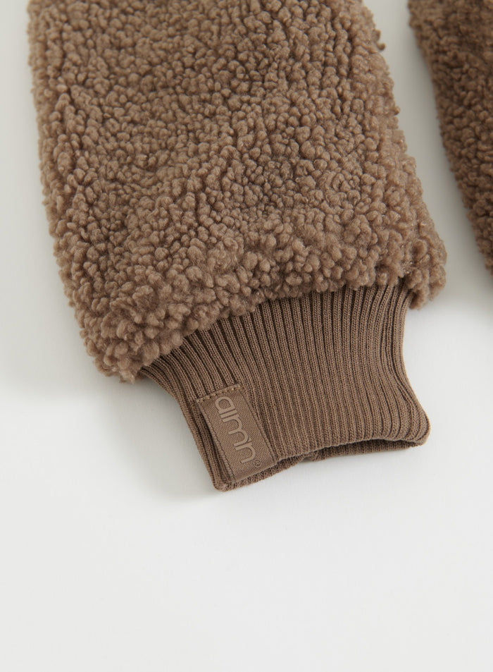 Flatlay detail of hazelnut pile mittens with visible brand tag
