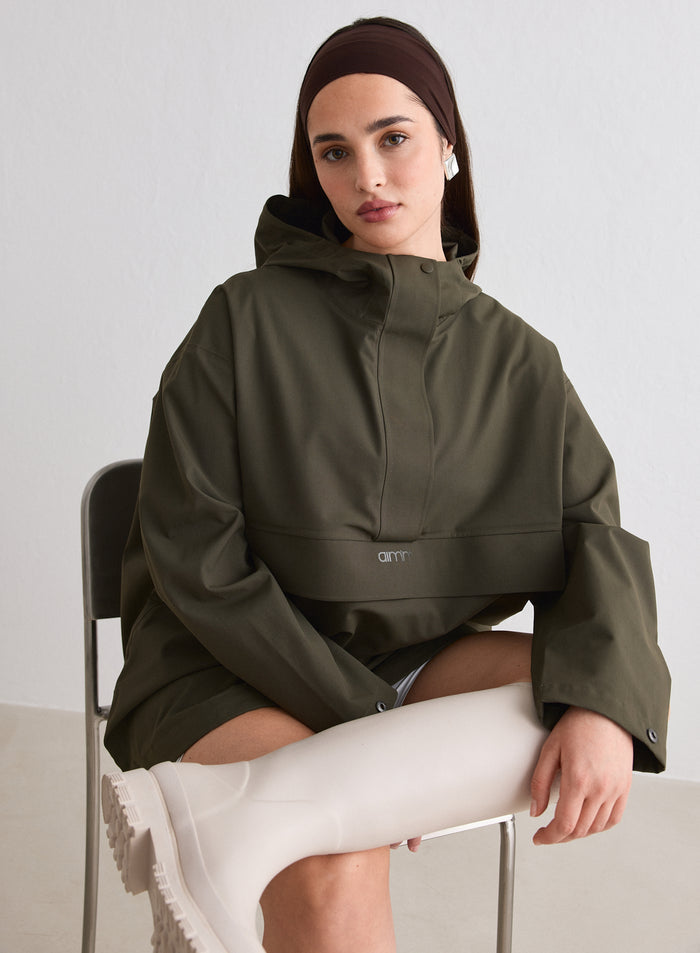 A model sitting on a chair wearing a Khaki Waterproof Oversized Anorak from aim'n and beige boots [M-174cm]