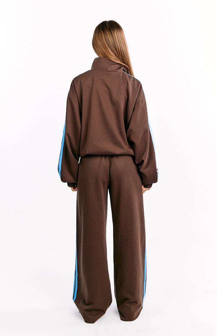 Rear view of chocolate brown wide-leg track pants with blue stripes down the side seams, worn with a matching track jacket