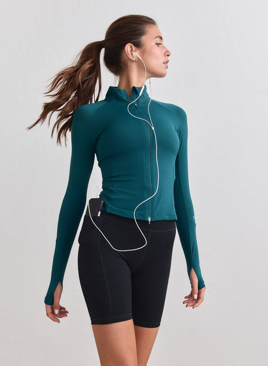 Lagoon teal aim'n Running Zip Long Sleeve with a half-zip and thumbholes, worn with black shorts. [M-178cm]