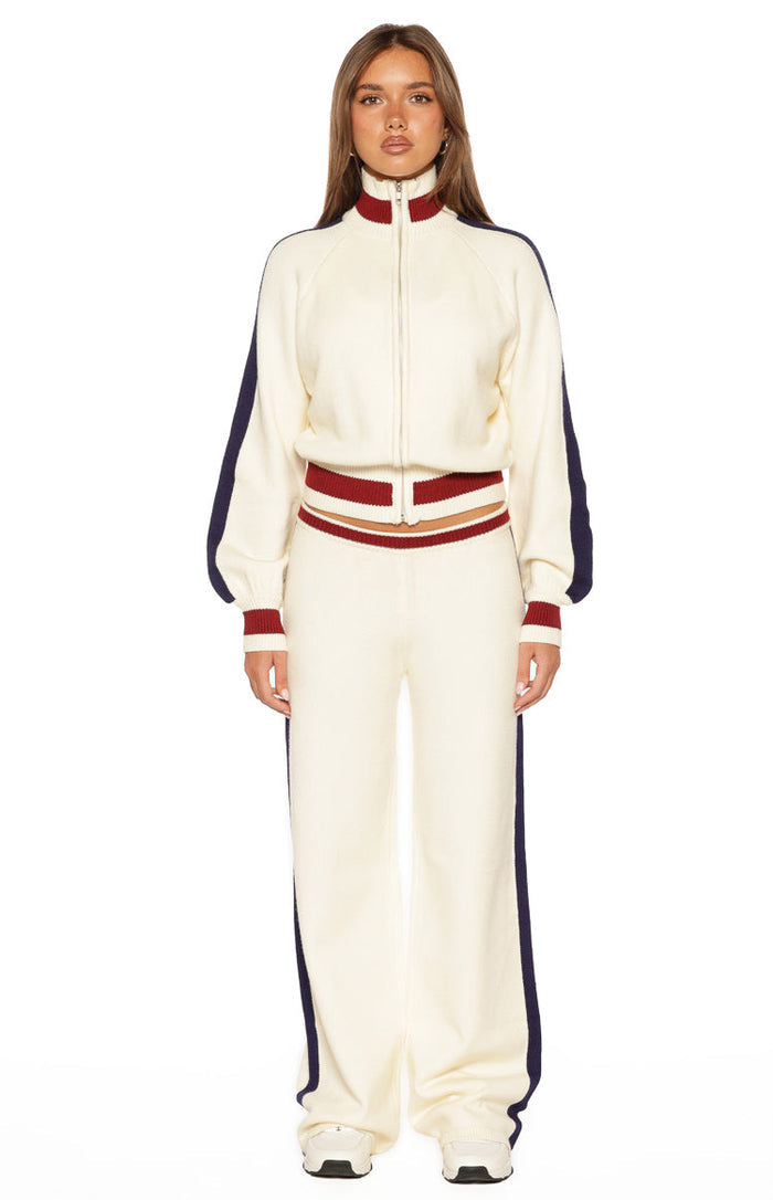 Front view of a cream knit zip sweater with a high red and cream ribbed collar, full zip, navy stripe long sleeves, and striped ribbed hem