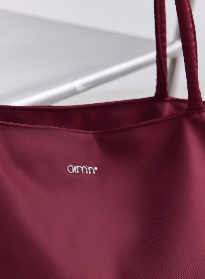 Merlot nylon tote bag detail showing the smooth fabric texture and a silver aim'n logo.