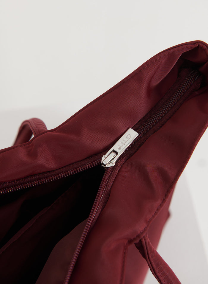 Close-up of a merlot nylon tote bag showing the silver zipper with aim'n branding.