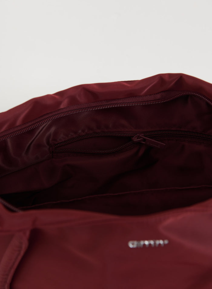 Interior of a merlot nylon tote bag featuring a zippered pocket and metallic aim'n logo.
