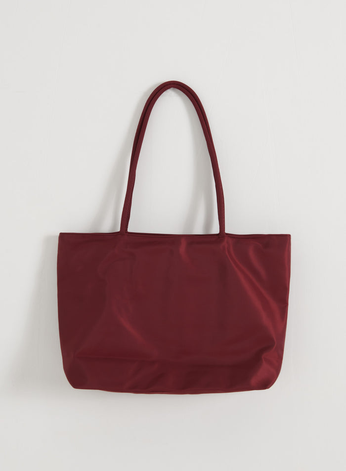 Merlot nylon tote bag by aim'n with long shoulder straps and a smooth finish against a white wall.