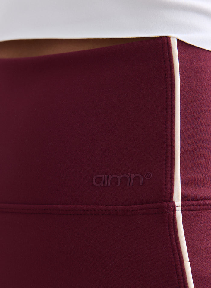 Close-up detail of the merlot Sense Contrast Skort with white side piping and a tonal aim'n logo. [XS-165cm]