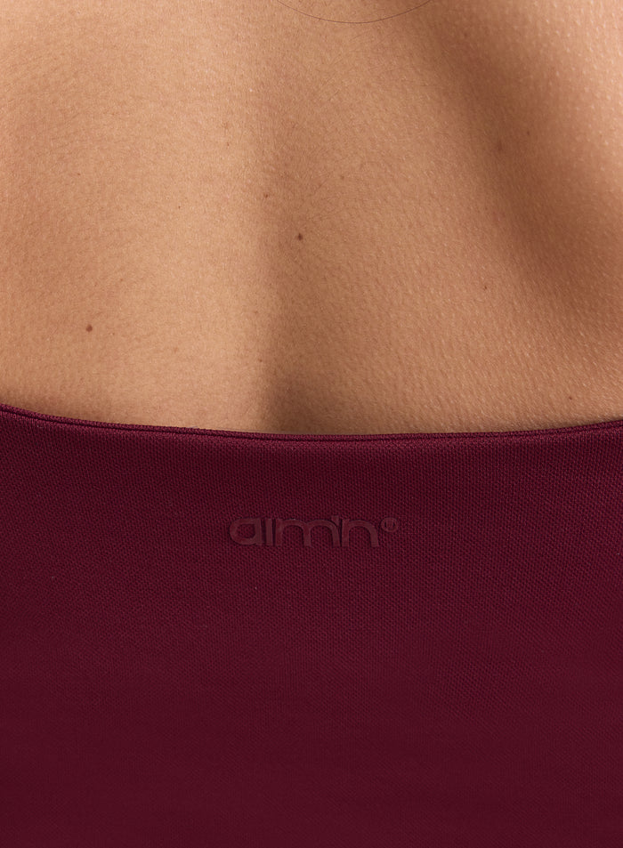 Close-up of the embossed aim'n logo on the back of a merlot Shape Seamless Strap Singlet. [XS-165cm]