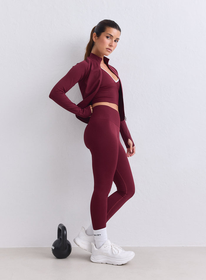 A model wears merlot aim'n high-waisted Shape Seamless Tights with a matching jacket in a gym setting. [XS-165cm]