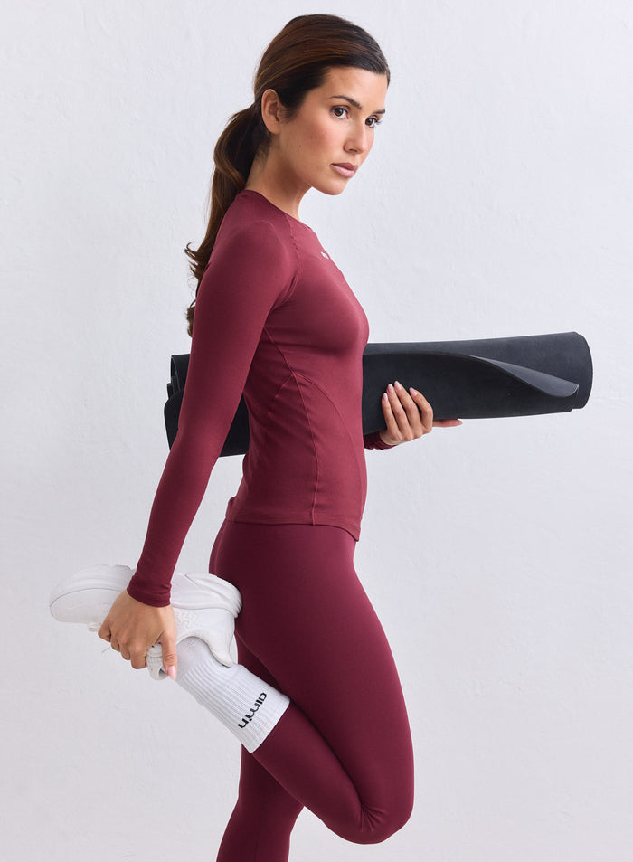Merlot Soft Basic Long Sleeve by aim'n worn by a woman holding a black yoga mat and stretching. [S-165CM]