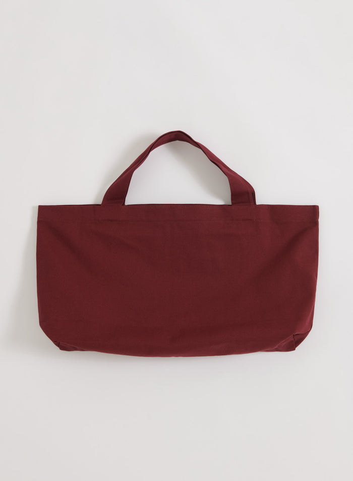 Rich merlot aim'n Varsity Tote Bag in a woven cotton fabric, shown in a flatlay view.