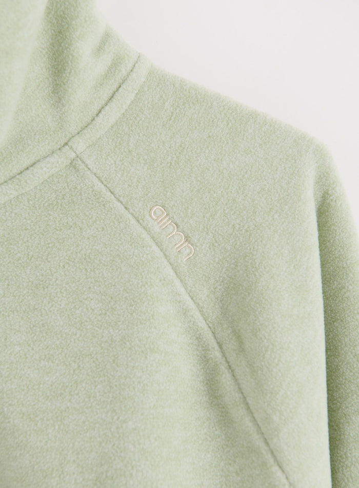 Close-up of the pistachio fleece zip jacket showing the embroidered aim'n logo on the shoulder