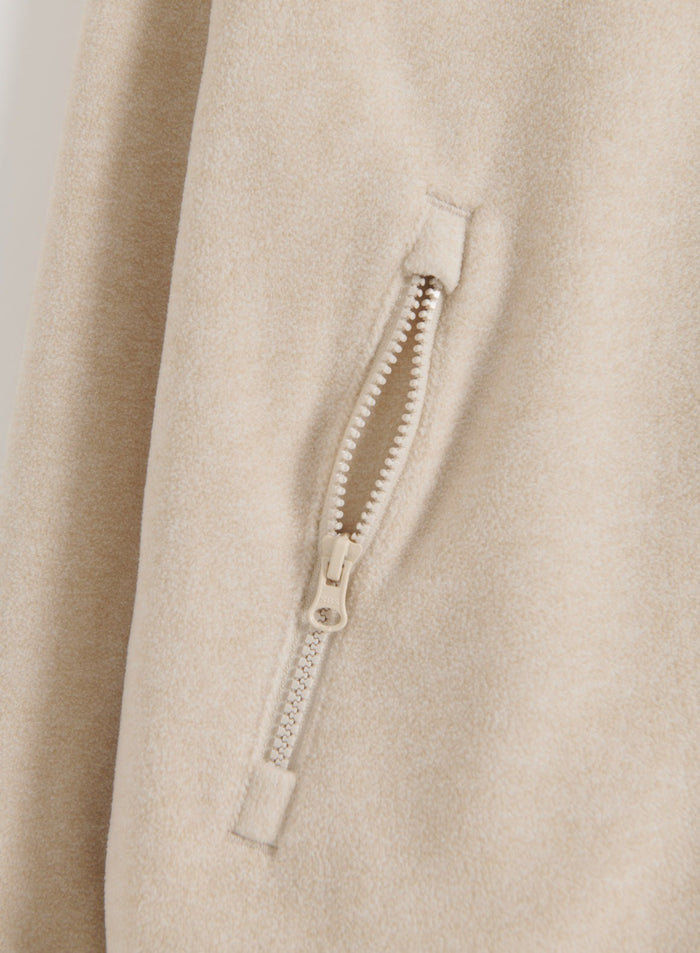 Close-up of the sand fleece jacket’s zip pocket and soft fleece fabric