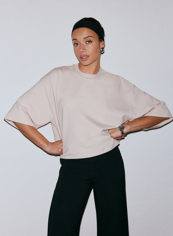 Model wearing a sand-colored Luxe Boxy Short Sleeve top and black pants, hands on hips [M-170cm]