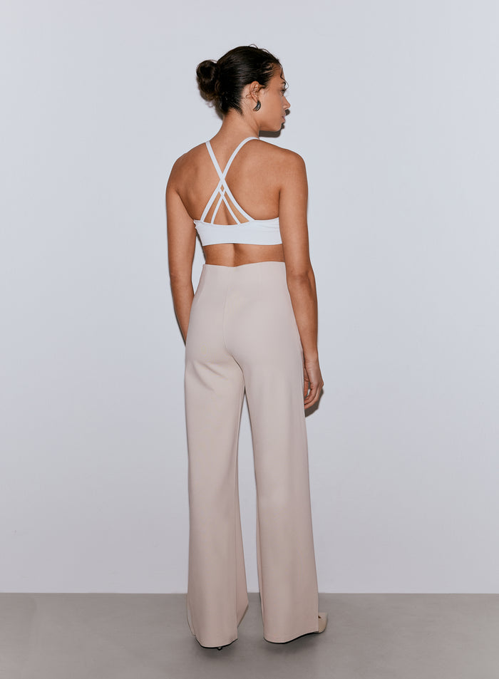 Woman seen from the back wearing sand wide-leg Luxe Pants and a white multi-strap sports bra [36-170CM]