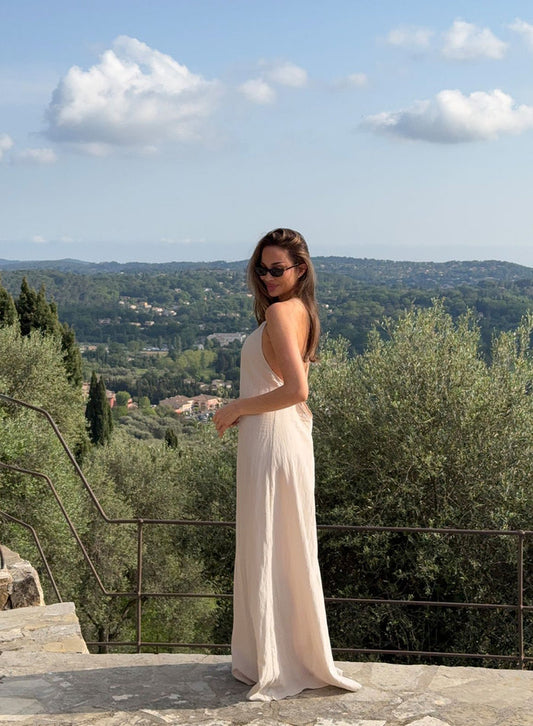 Sand Riviera Maxi Dress by aim'n featuring a flowy silhouette and thin straps, styled on a scenic terrace.