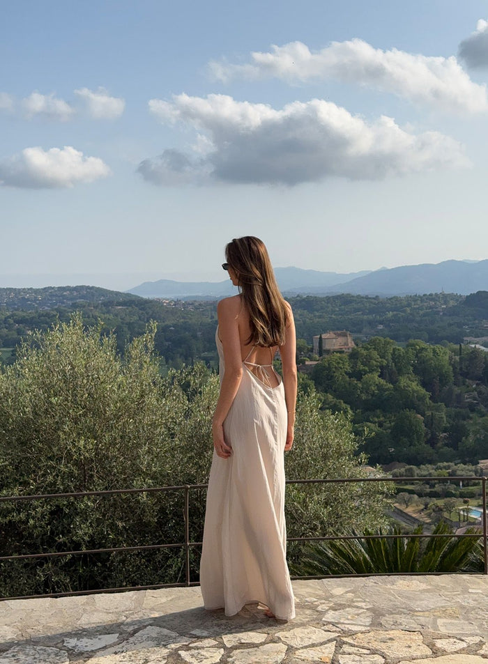Sand Riviera Maxi Dress with thin straps and low-cut back, worn in a scenic outdoor landscape by aim'n.