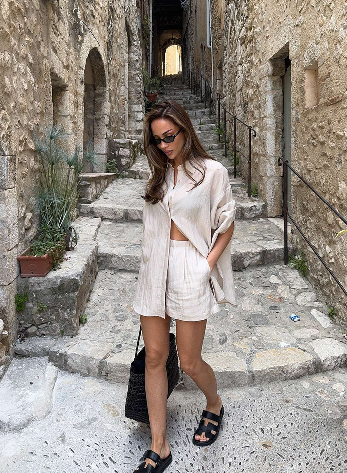 Sand Riviera Shirt and matching shorts by aim'n worn by a woman walking through a rustic stone alleyway.