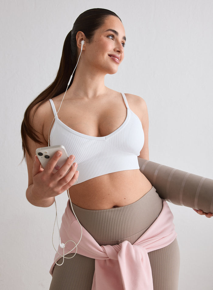 A woman wearing a White Ribbed Seamless Deep Cut Bra from aim'n holding a yoga mat and phone [L-174cm]