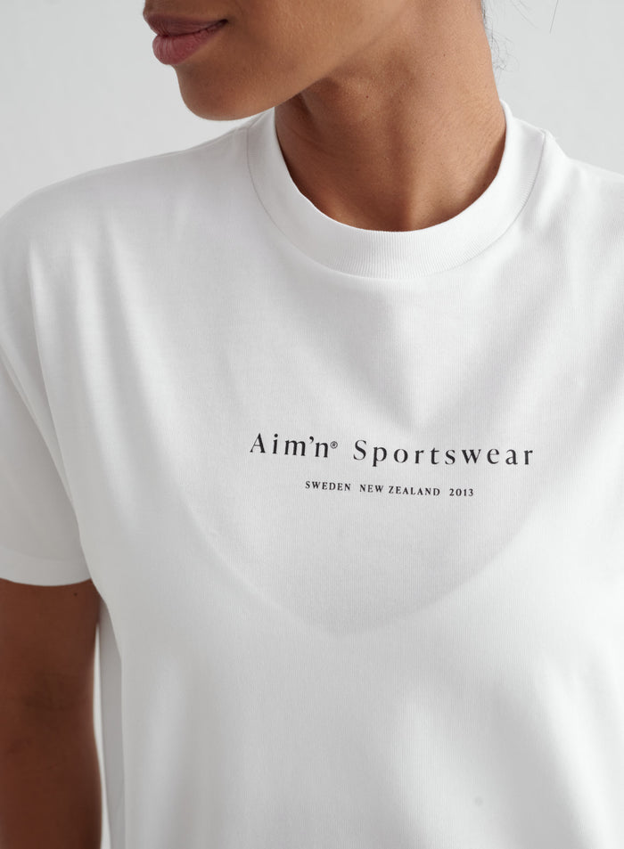 White aim'n Serif Boyfriend T-shirt featuring a black serif logo printed on the chest.